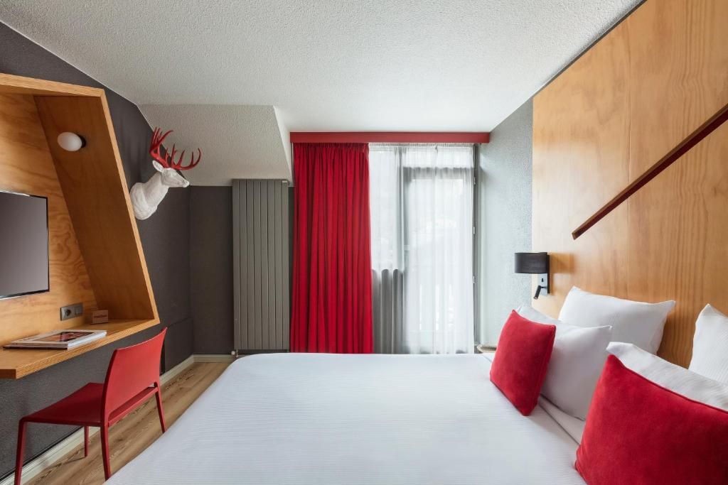 Une chambre au bois clair et rideaux rouges, avec son bureau et sa fenêtre sur le balcon