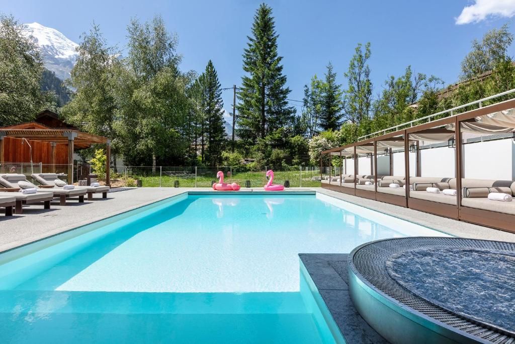 La piscine extérieure et son bain à remous rond, bordés de transats, avec les sommets au fond