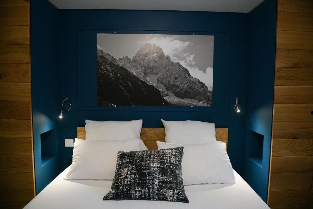 Une chambre à mur bleu et paroi de bois, avec une grande photographie de montagne au-dessus du lit