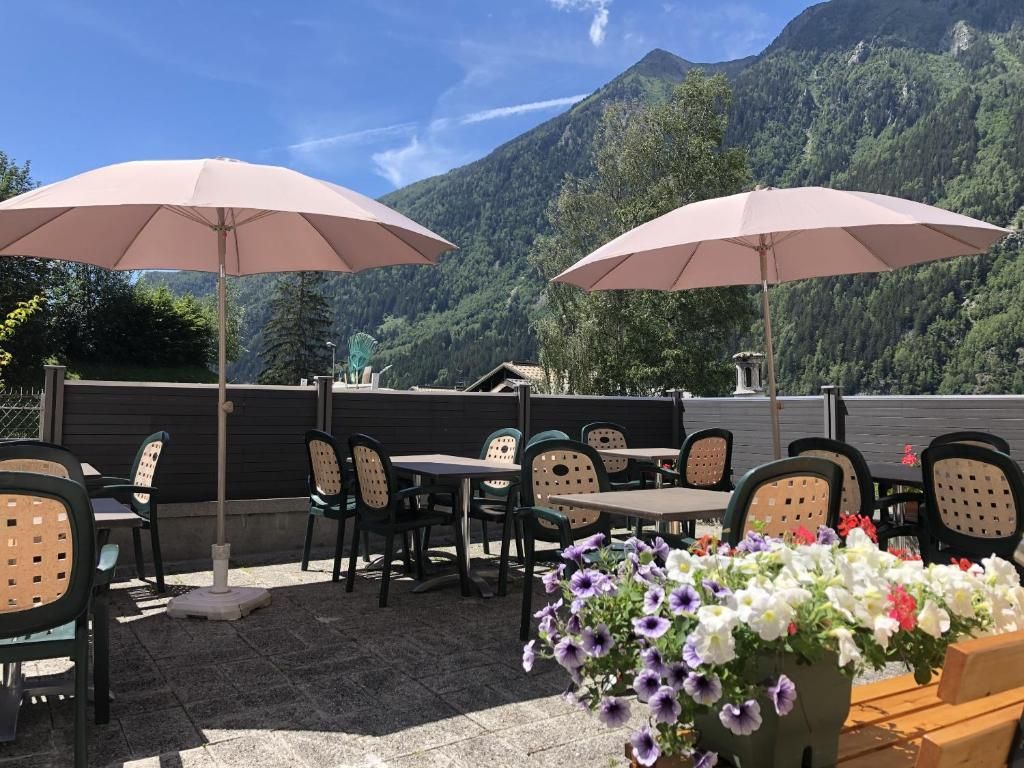 La terrasse et ses tables sous deux parasols, avec ses jardinières fleuries et le versant boisé au fond