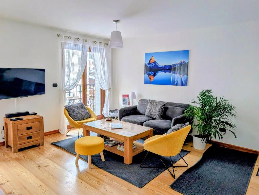 Le séjour clair de l’appartement, avec son canapé gris, ses fauteuils jaunes et la porte-fenêtre du balcon