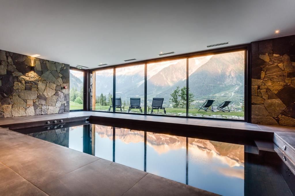 La piscine intérieure au bord d’une paroi entièrement vitrée, avec le versant qui se reflète sur l’eau