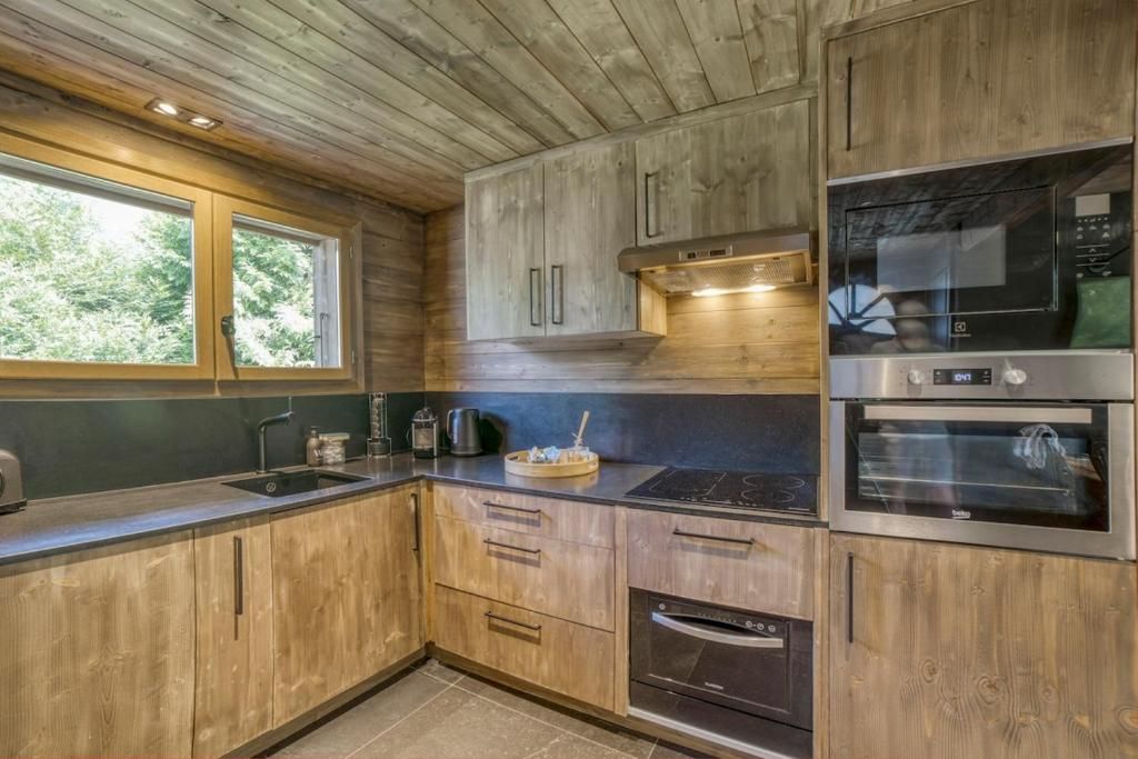 La cuisine équipée du chalet, en bois clair, avec plaques, four et lave-vaisselle sous la fenêtre