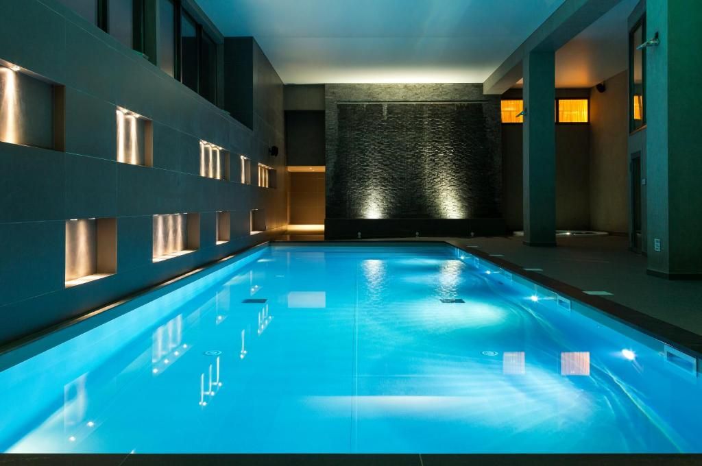 La piscine intérieure éclairée en bleu, bordée de murs sombres percés de niches lumineuses