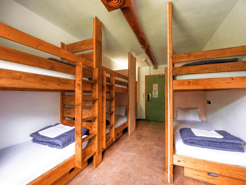 Un dortoir avec ses lits superposés de bois clair, ses serviettes pliées et sa porte verte
