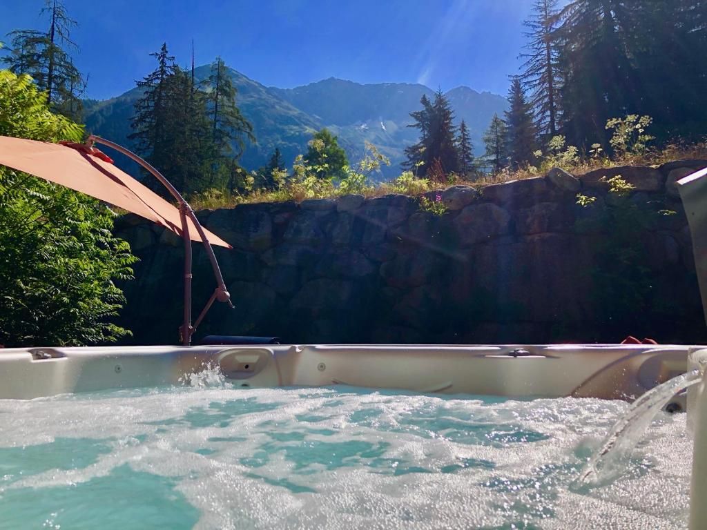 Le bain à remous encastré dans un plancher de bois, sous une verrière ouverte sur les sapins