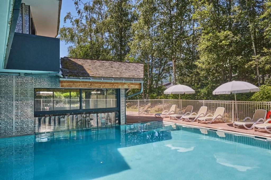La piscine extérieure et ses transats, bordée de parasols, devant le bâtiment de bois