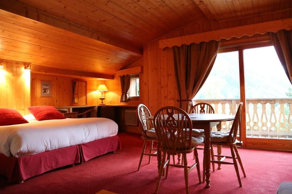 Une chambre lambrissée de bois, avec son grand lit à couverture rouge et ses lampes de chevet