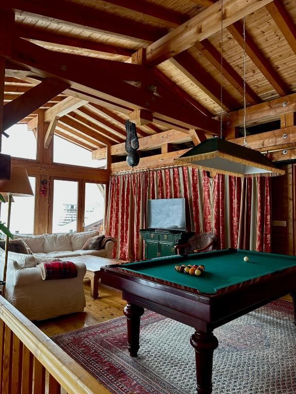 Le salon commun sous ses grandes poutres, avec son billard, ses canapés et ses baies vitrées sur la forêt
