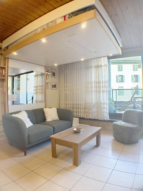Le séjour avec son canapé gris, sa table basse et les voilages de la porte-fenêtre du balcon