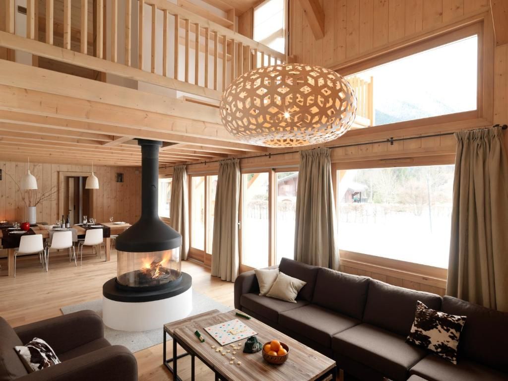 Le séjour d’un chalet, avec son poêle suspendu au centre, ses canapés et la baie vitrée sur le jardin