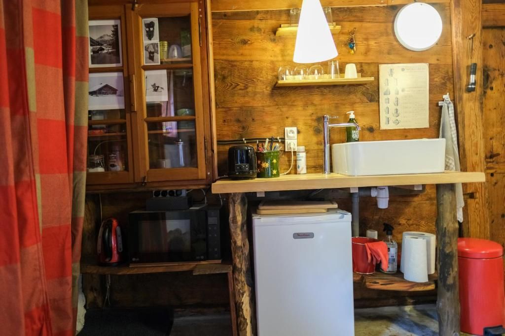 Le coin cuisine adossé au vieux bois, avec son évier, son réfrigérateur et ses étagères garnies