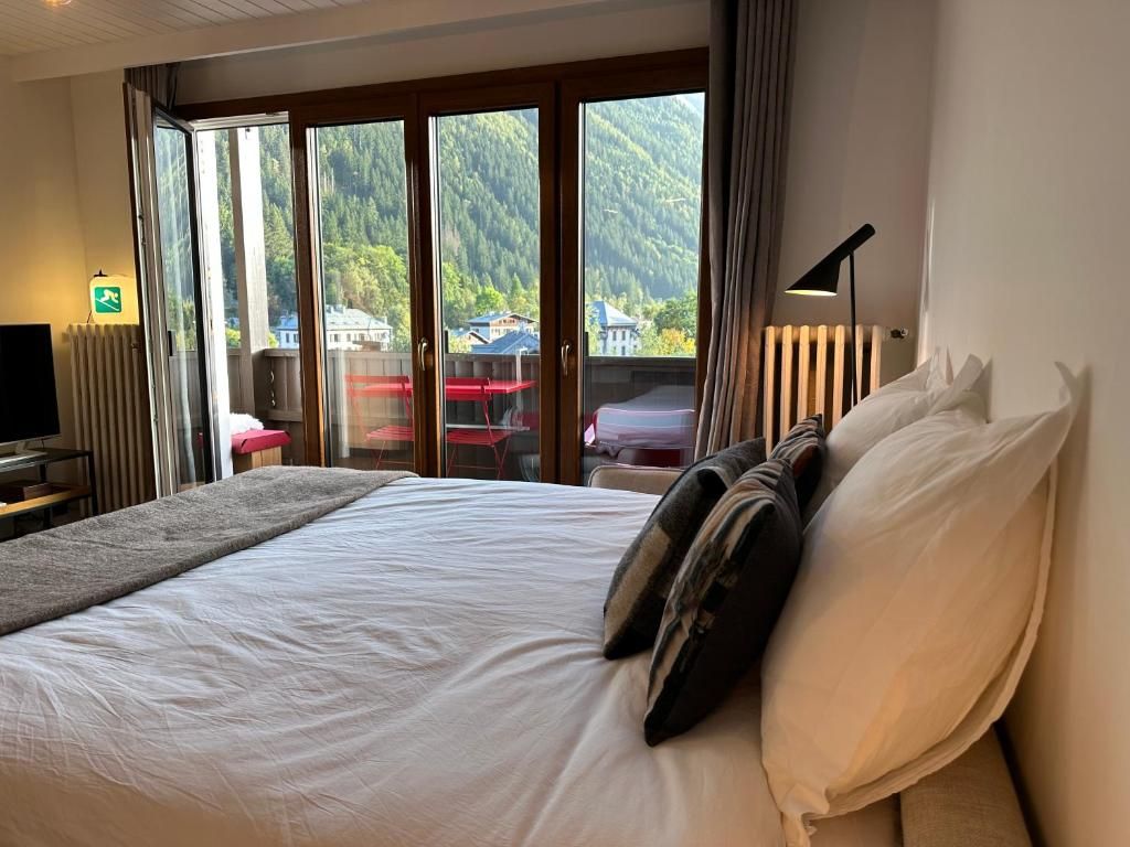 Une chambre ouverte sur la porte-fenêtre du balcon, avec son grand lit et la forêt visible au dehors