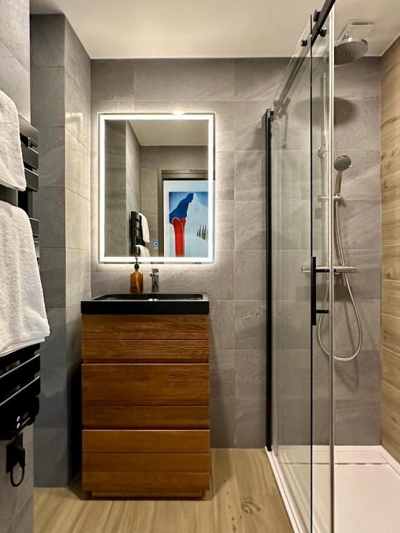 La salle de bains, avec sa douche à l’italienne, son plan vasque noir et son miroir rétroéclairé