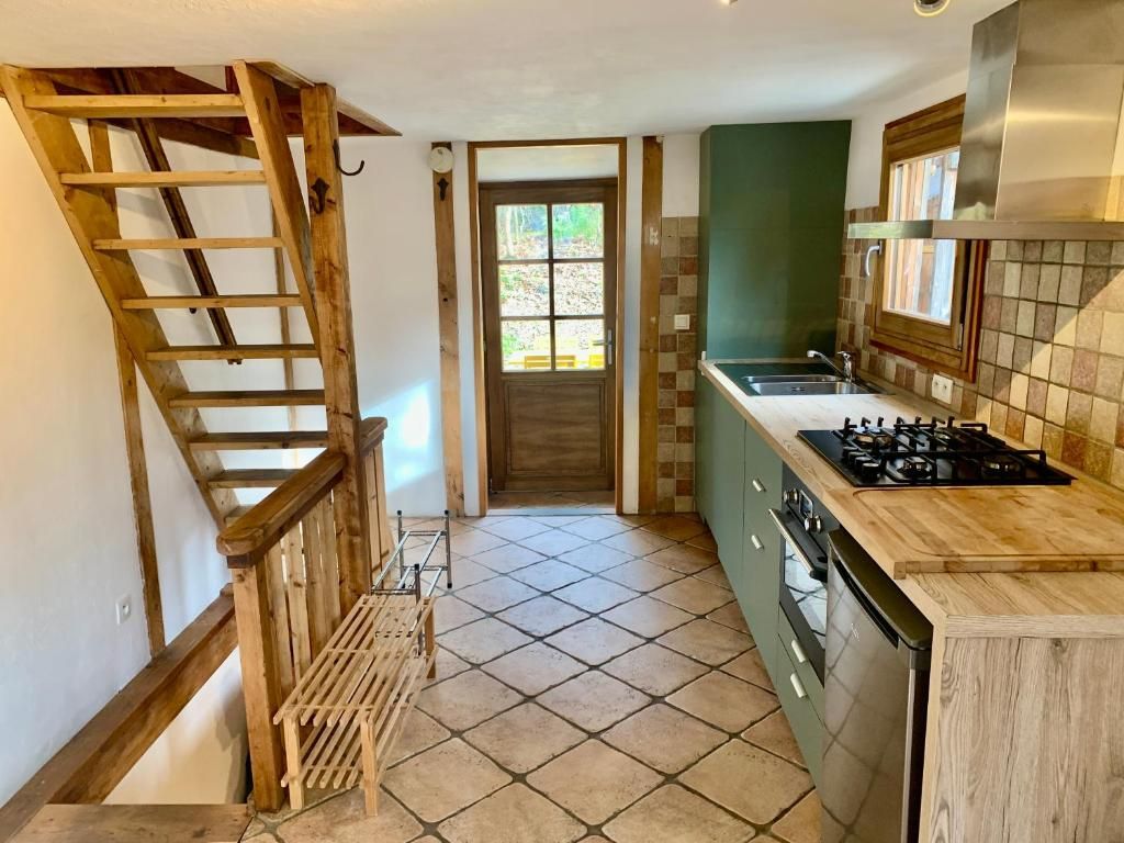 L’entrée carrelée avec son escalier de meunier et le plan de cuisine qui court le long du mur