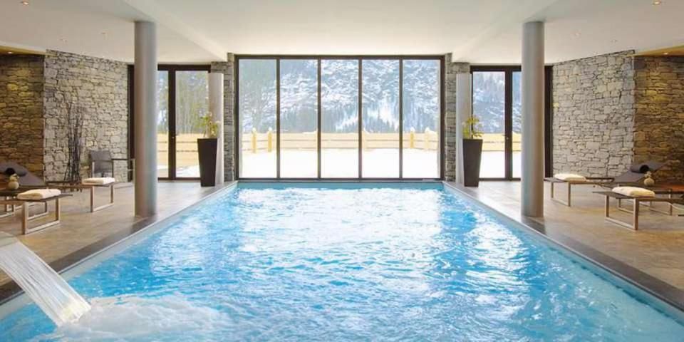 La piscine intérieure, longue et éclairée, derrière une paroi vitrée ouverte sur la forêt
