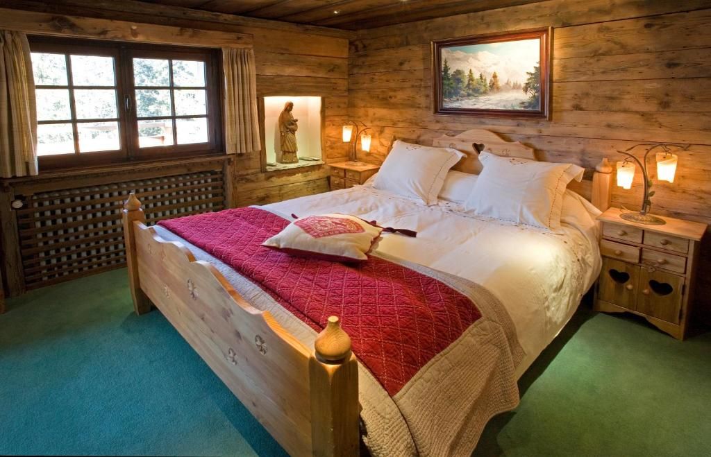 Une chambre de vieux bois éclairée aux appliques, avec son lit à couverture rouge et son tableau ancien