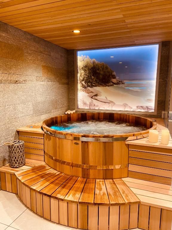Le bain à remous en bois, rond, dans sa pièce lambrissée, devant une grande photographie de montagne