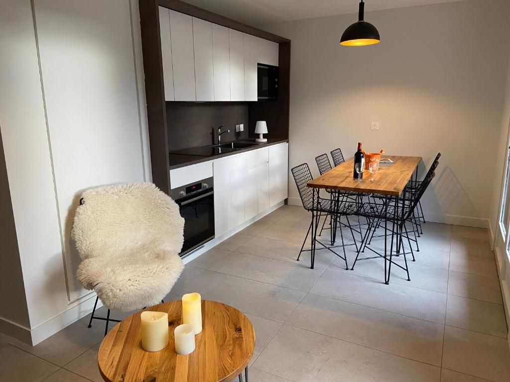 La cuisine ouverte d’un appartement, avec son plan de travail blanc et sa grande table de bois