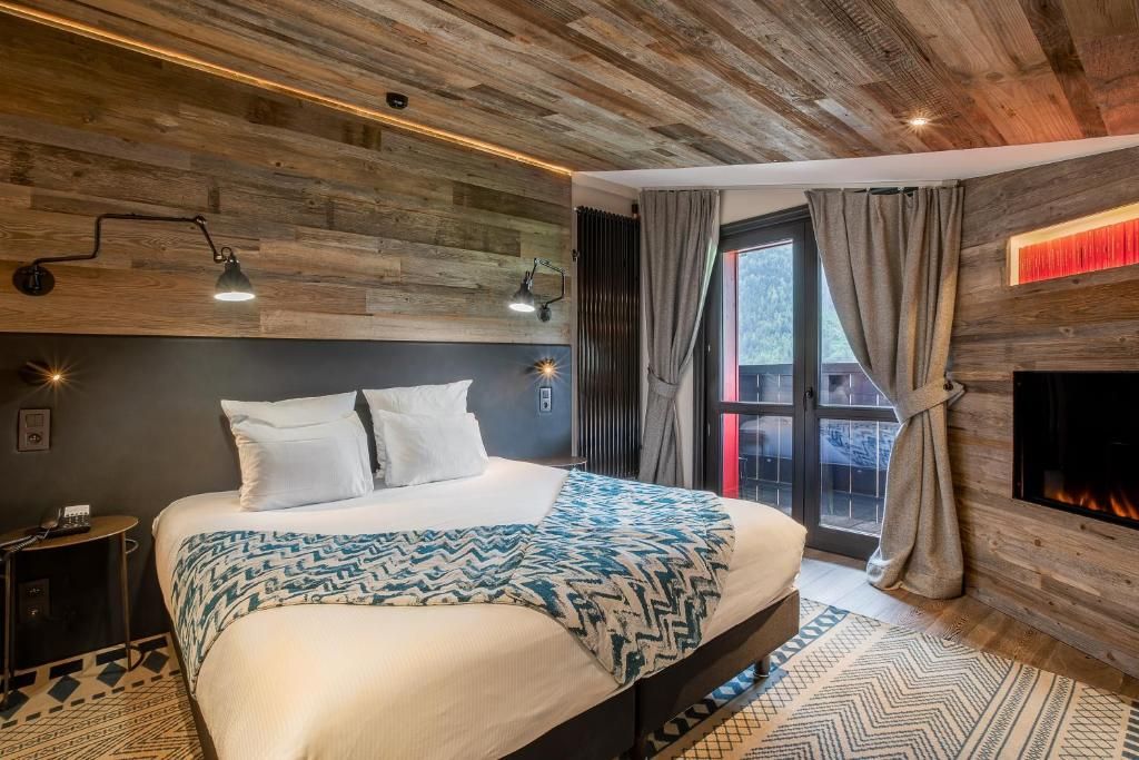 Une chambre habillée de vieux bois, avec sa cheminée, son lit double et la porte-fenêtre du balcon