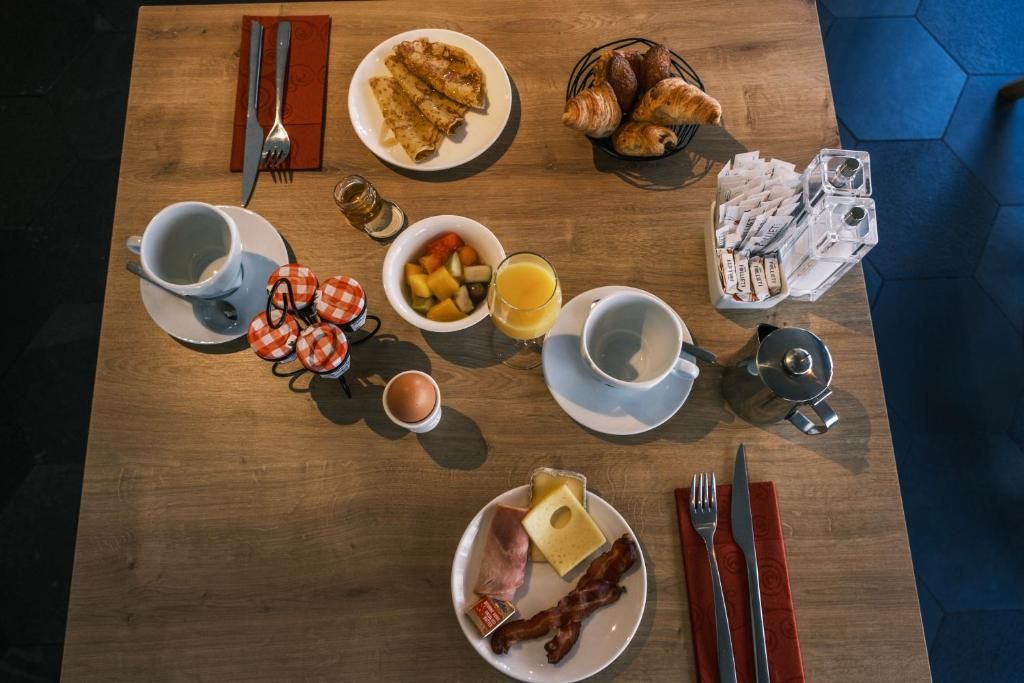 Une table de petit-déjeuner vue du dessus, avec viennoiseries, œuf, bacon et jus d’orange
