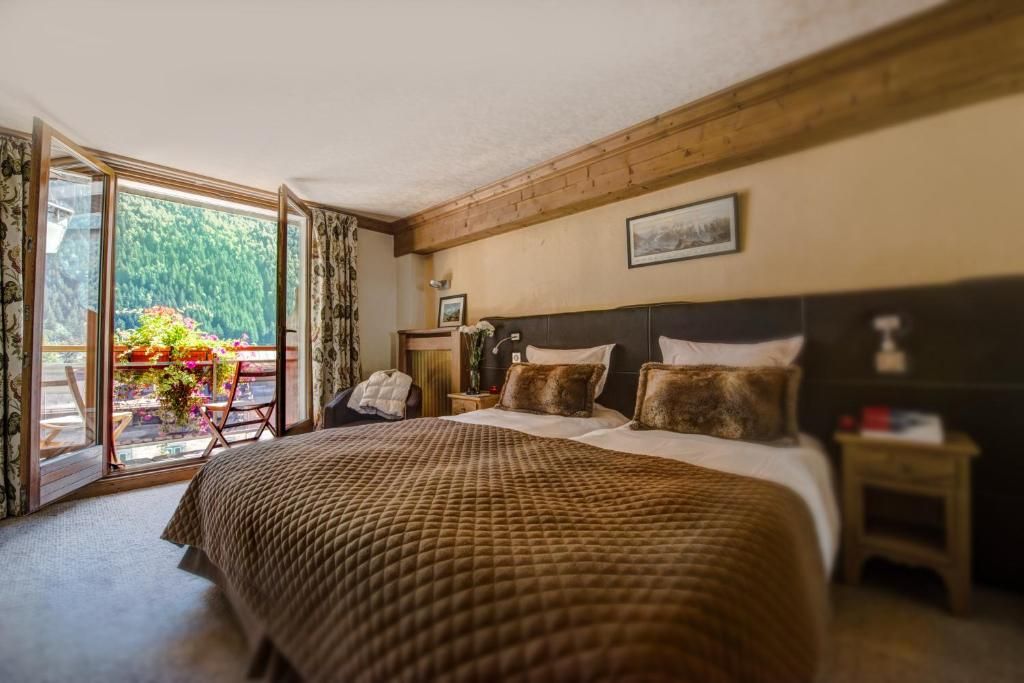 Une chambre au plafond mansardé, avec son grand lit et sa baie ouverte sur le balcon
