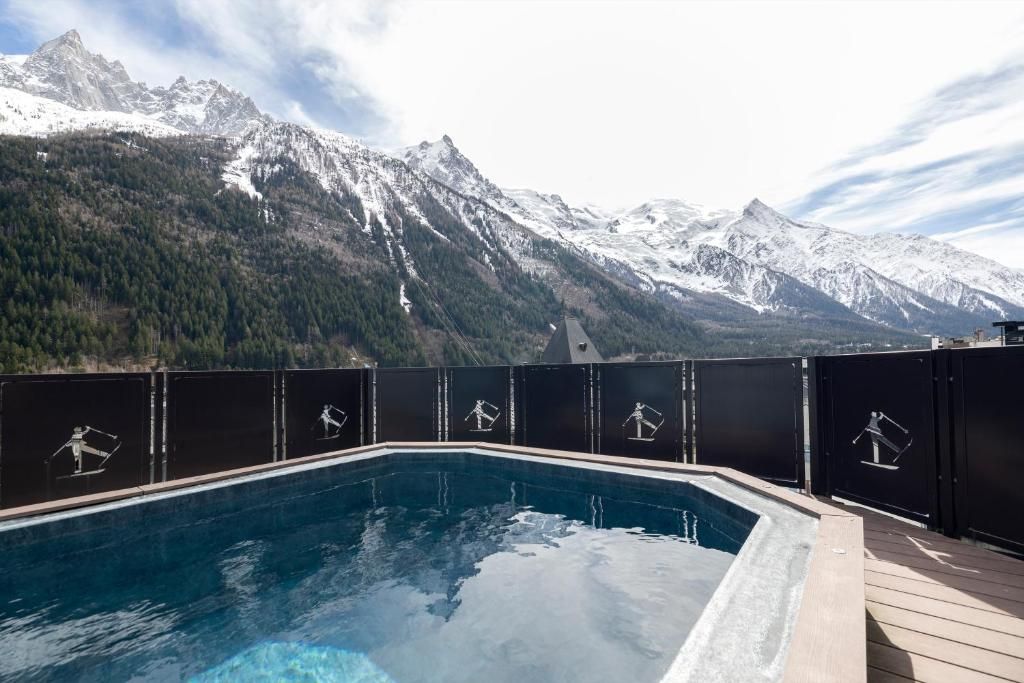 La piscine extérieure du toit, bordée d’une paroi sombre, avec les sommets enneigés au fond