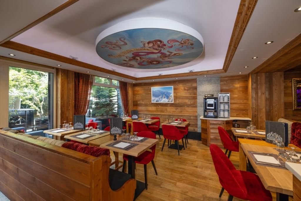 La salle de restaurant lambrissée, ses tables dressées, ses chaises rouges et sa fresque au plafond